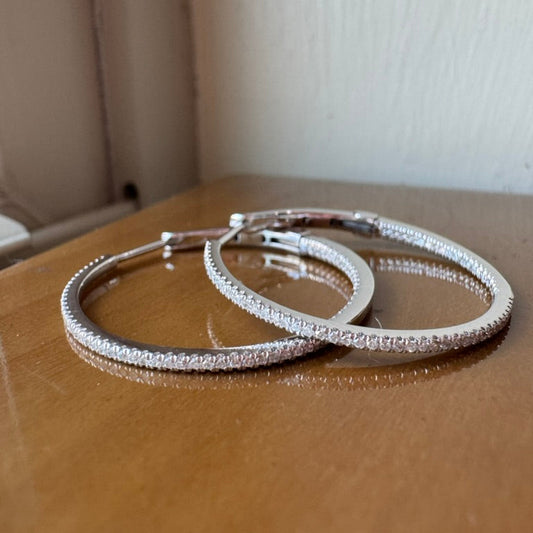 Pair of silver hoop earrings on a wooden surface with a white background