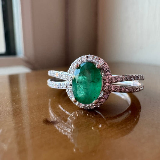 Ring with a green emerald and diamond accents on a reflective surface