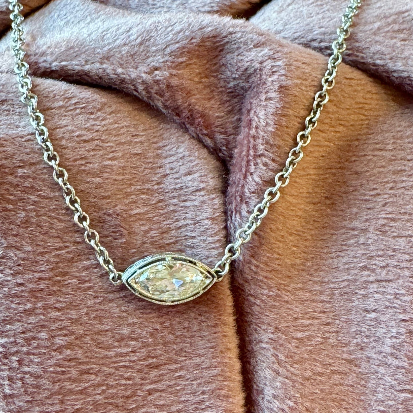 white gold necklace with a diamond pendant on a pink fabric background