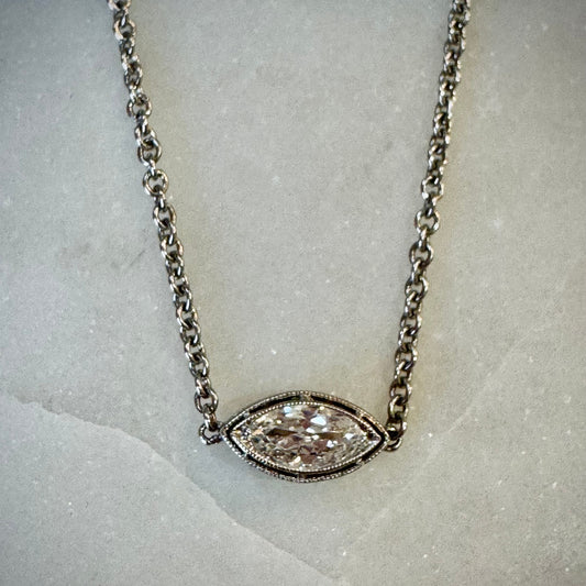 White gold necklace with a marquise-shaped diamond pendant on a marble surface.