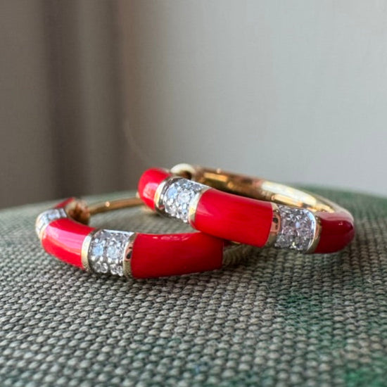 Red earrings with gold and diamond accents on a textured surface