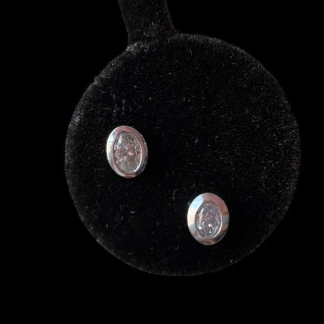 Pair of white gold earrings on a black round cushion with a black background