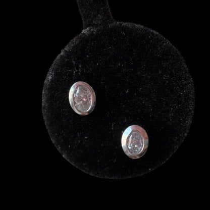 Pair of white gold earrings on a black round cushion with a black background