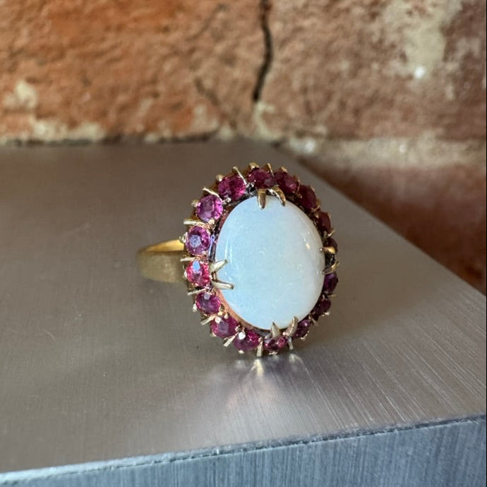 Ring with a large opal and ruby halo on a metallic surface with a brick background