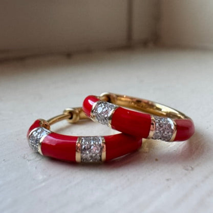 Red hoop earrings with gold accents on a light surface.