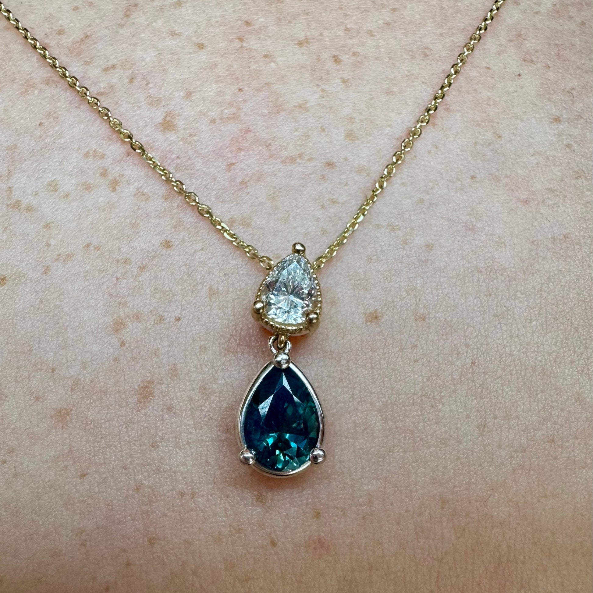 Gold necklace with a blue teardrop pendant on a person's neck.