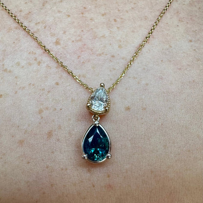 Gold necklace with a blue teardrop pendant on a person's neck.