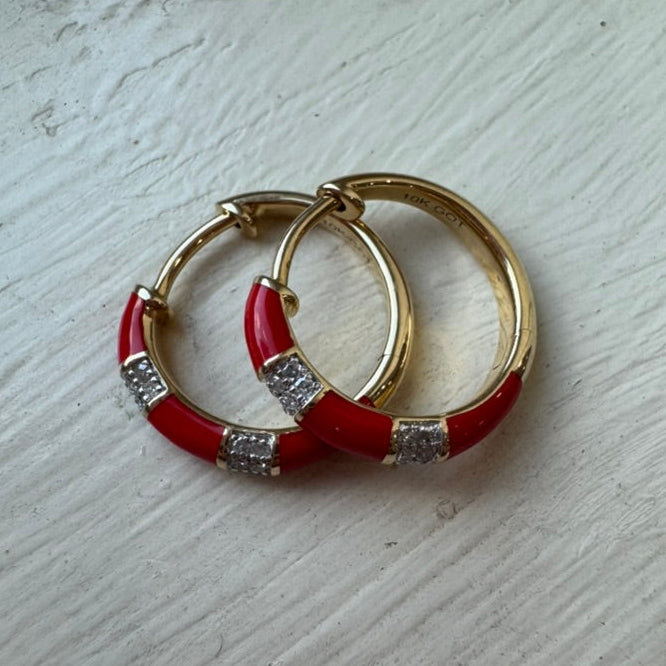 Gold hoop earrings with red enameled bands and embedded diamonds on a light wooden surface.