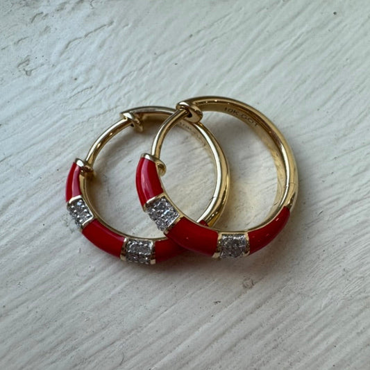 Gold hoop earrings with red enameled bands and embedded diamonds on a light wooden surface.