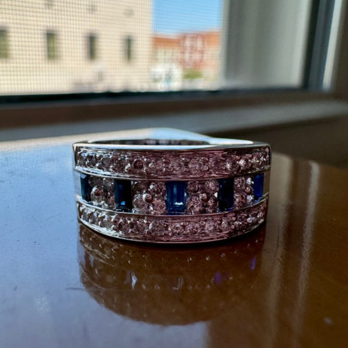Silver ring with blue gemstones on a reflective surface with a window background