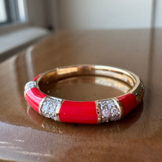 Gold ring with red enamel band and diamond-like stones on a wooden surface