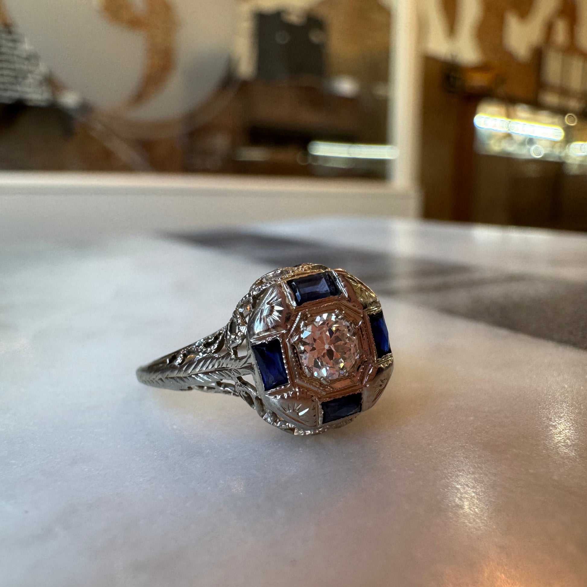 Close-up of a diamond ring with sapphires on a white surface.